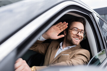happy man in glasses looking through car window and waving hand while driving auto © LIGHTFIELD STUDIOS