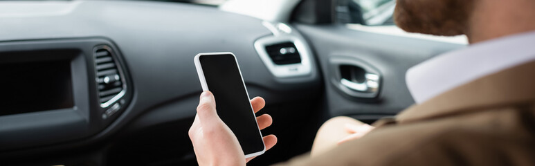 cropped view of blurred man holding smartphone with blank screen in car, banner