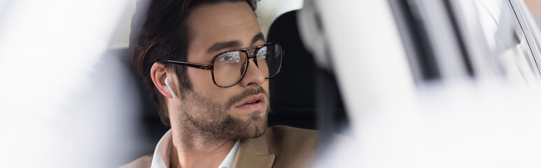 businessman in glasses and wireless earphones in car, banner
