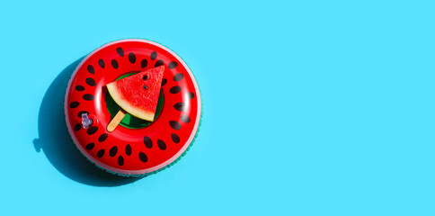 Watermelon slice popsicle on swim ring toy on blue background. Summer background concept