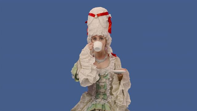 Portrait of courtier lady in white vintage lace dress and wig, drinking coffee from a cup. Young woman posing in studio with blue screen background. Close up. Slow motion ready 59.94fps.