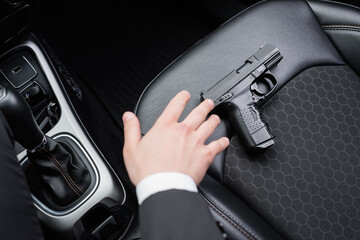 top view of bodyguard reaching gun on seat of modern automobile