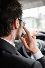 back view of bodyguard in sunglasses pointing at security earpiece while driving modern automobile