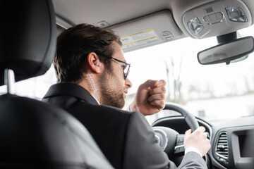 bearded bodyguard in sunglasses and security earpiece talking while driving modern automobile