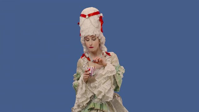 Portrait of courtier lady in white vintage lace dress and wig, enjoying delicious fries. Young woman posing in studio with blue screen background. Close up. Slow motion ready 59.94fps.