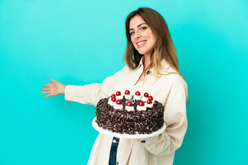 Caucasian woman holding birthday cake isolated on blue background extending hands to the side for inviting to come