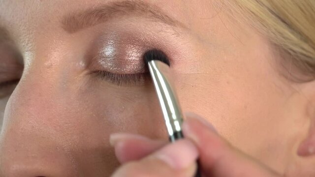 A client in a beauty salon does makeup. The hand of a professional makeup artist draws shadows on the eyes on the eyelid with a brush. Selects them. actor or actress is applied makeup in dressing room