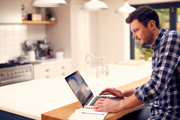 Man Working From Home Using Laptop On Kitchen Counter