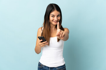 Fototapeta na wymiar Young caucasian woman using mobile phone isolated on blue background showing and lifting a finger