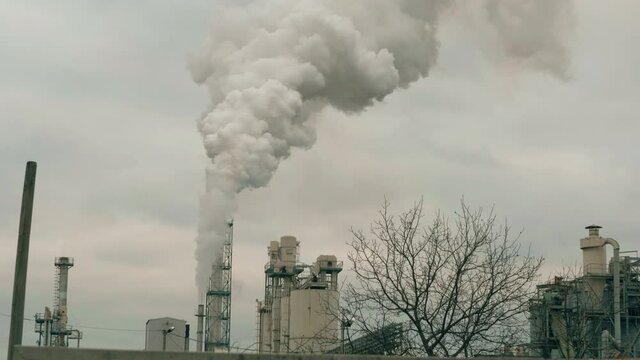 Factory chimney. Puffs of smoke coming out of a tall smokestack in a production facility. Environmental pollution problems.