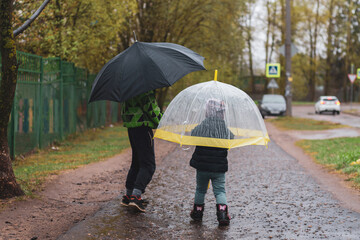 Brother and sister walk under umbrellas in rainy weather on the street home