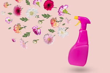 Creative minimal idea made from a bottle with a spray and various flowers flying in the air on a light pink background.