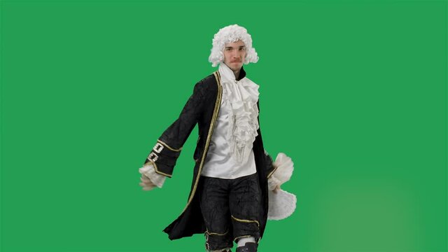 Portrait of courtier gentleman in black historical vintage suit and white wig, dancing merrily with a fan in his hands. Young man posing in studio with green screen background. Slow motion.