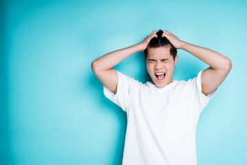 Young vietnamese man in white t-shirt grabs his head with his hands and gets angry