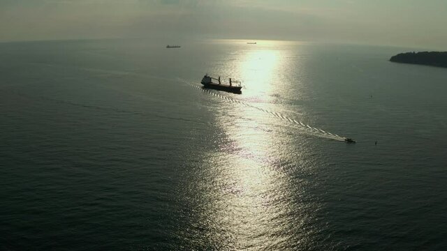 Cargo ship calling into the port under the guide of tugboat. Sunset lights the sea and the ship.  