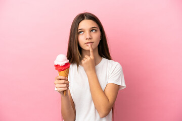 Little girl with a cornet ice cream over isolated pink background having doubts while looking up