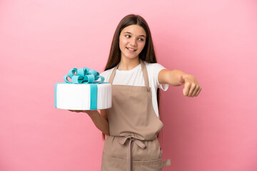 Little girl with a big cake over isolated pink background giving a thumbs up gesture