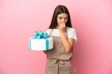 Little girl with a big cake over isolated pink background having doubts