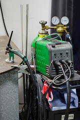 Tig welder with a torch in a stand and bottles in the background.