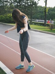 young woman goes in for sports in the stadium, running, jumping rope, warm-up and stretching