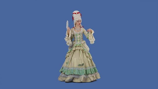 Portrait of courtier lady in white vintage lace dress and wig is waving a fan and curtsy. Young woman posing in studio with blue screen background. Full lenght. Slow motion.