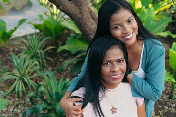 Portrait of African American mother with daughter in garden, smiling at camera and hugging. Family...
