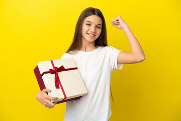 Little girl holding a gift over isolated yellow background celebrating a victory