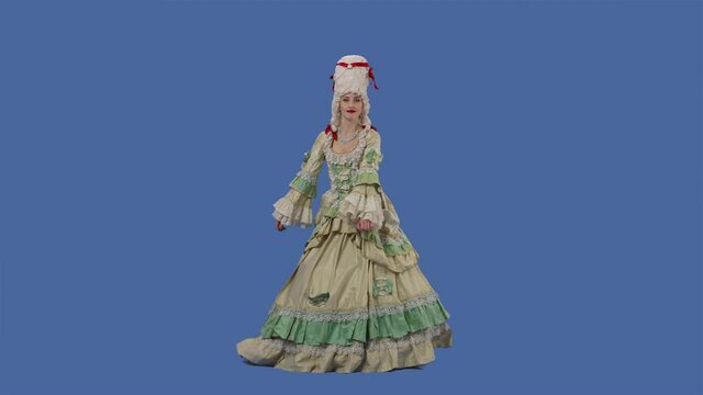 Portrait of courtier lady in white long vintage lace dress and wig is dancing merrily. Young woman posing in studio with blue screen background. Full lenght. Slow motion.