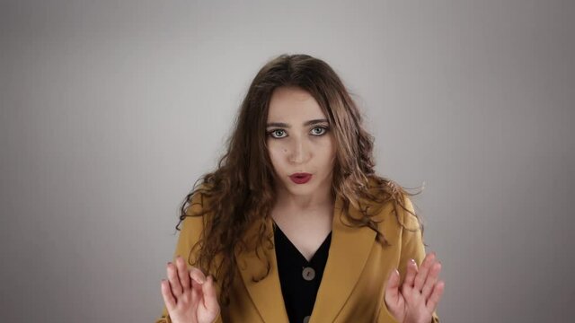 Young caucasian woman is showing ok sign and breathing out to calm down in slowmo. Isolated portrait of lady with long curly hair who tries to balance her mental condition. Concept of people emotions.