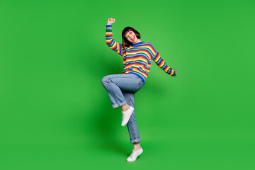 Full length photo of adorable lucky young woman wear striped sweater smiling rising fists isolated green color background
