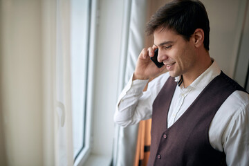 young caucasian male talking on a cell phone by the window, smiling