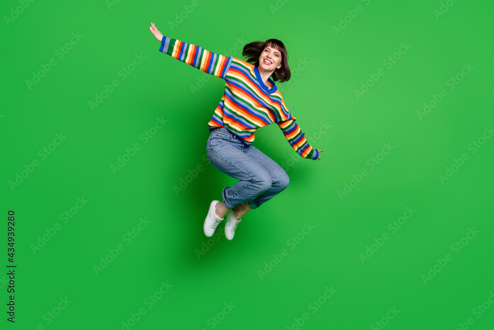 Sticker Full length photo of cute pretty young woman wear striped sweater smiling jumping high arms sides isolated green color background