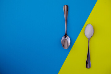 Sugar-replacement tablet of stevia and sugar in tea spoons lying in opposite directions on bright...