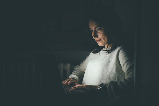 Young woman indoors at home using computer late at night finishing deadline project doing business overtime