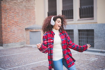 Young multiethnic woman outdoor listening music holding smartphone dancing enthusiastic