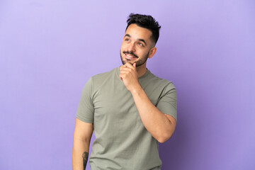 Young caucasian man isolated on purple background looking up while smiling