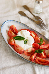 Traditional Italian salad with Burrata cheese, tomatoes and fresh basil. Mozzarella burrata salad with basil leaves and tomatoes on plate on beige linen tablecloth