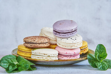Tender, delicious macaroon cakes on a green ceramic saucer and fresh mint leaves next to them.