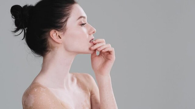 A side view of an attractive half naked woman is posing to the camera standing isolated over gray wall in the studio. Diversity tolerance. Every body is beautiful