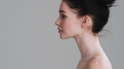 A beautiful half naked woman is turning her head to the camera standing isolated over gray wall in the studio. Diversity tolerance. Every body is beautiful