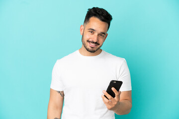 Young caucasian man isolated on blue background using mobile phone