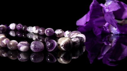 Purple amethyst beaded necklace on a black background with reflection. Energy stone, lilac jewelry...