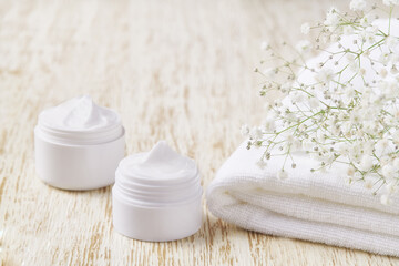 Obraz na płótnie Canvas Natural face cream or lotion, organic cosmetic to moisturize the skin with towel and flowers in the background.