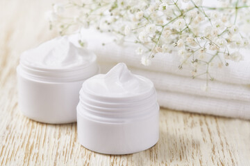Obraz na płótnie Canvas Natural face cream or lotion, organic cosmetic product to moisturize the skin with a towel and flowers on the background.