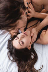 Blurred man touching sensual girlfriend with closed eyes on bed