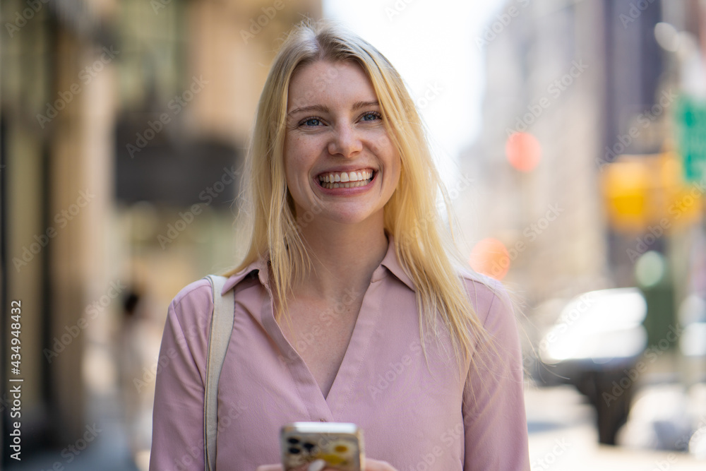 Poster Young caucasian woman in city walking street texting on cellphone