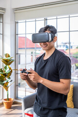 Young Asian man wearing virtual reality VR headset goggle holding controller playing futuristic game © wirojsid