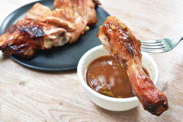 grilled chicken leg stabbing in silver fork dipping spicy sauce in cup