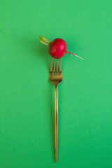 Radish impaled on a gold fork on the green  background. Location vertical.