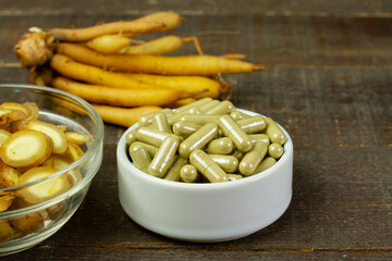 Finger root (Krachai) capsule in white bowl on rustic wooden background. The scientific name is Boesenbergia rotunda. Finger root is herb and Thai food ingredient.